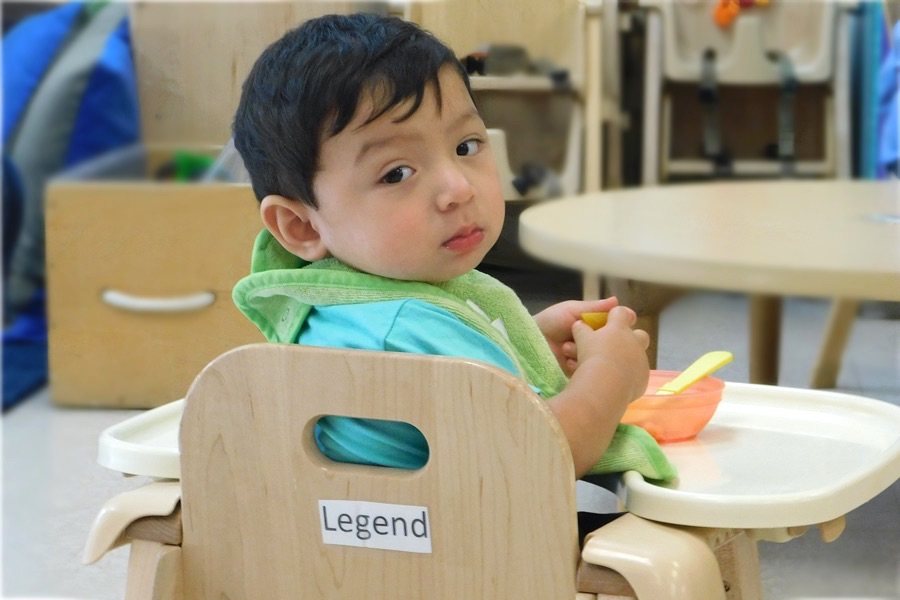kids-eating-legend-behind women in mask playing with infant baby in classroom daycare